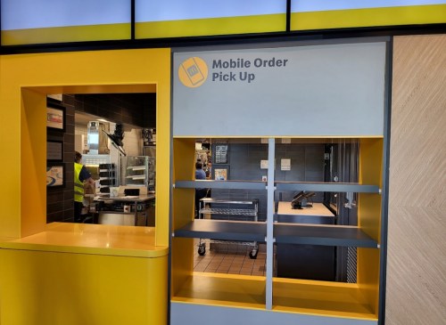 Mobile order pick-up area in a restaurant, featuring a service window and empty shelves.