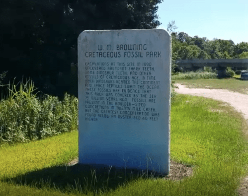 Stone monument with text about W. M. Browning Cretaceous Fossil Park and its fossil discoveries. Green trees in background.