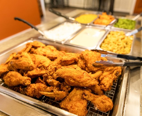 A tray of golden fried chicken wings with various sides in metal containers in the background.