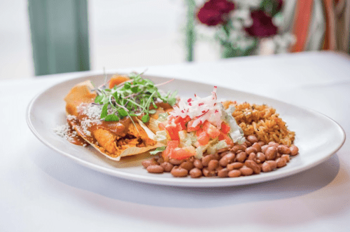 A plate of enchiladas topped with sauce, served with rice, refried beans, and a fresh salad.