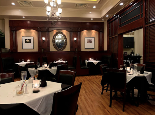Elegant restaurant interior with dark wood accents, white tablecloths, and empty tables set for dining.