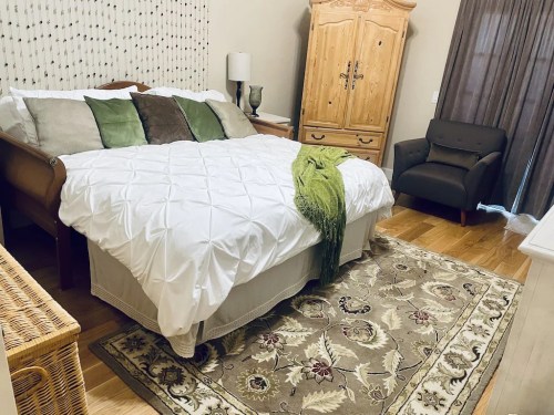 Cozy bedroom featuring a bed with white bedding, green accents, a wooden armoire, and a comfortable chair.