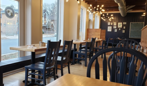 A cozy restaurant interior with wooden tables, chairs, and large windows, featuring warm lighting and a welcoming atmosphere.