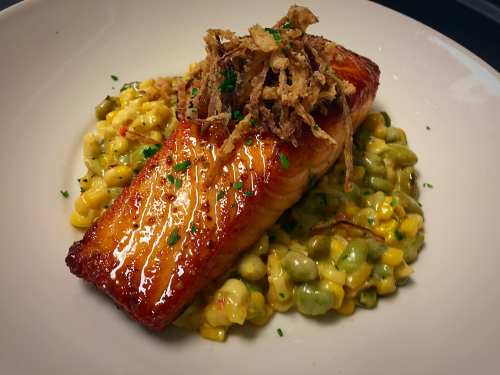 A beautifully plated salmon fillet on a bed of creamy corn and pea mixture, topped with crispy fried onions.