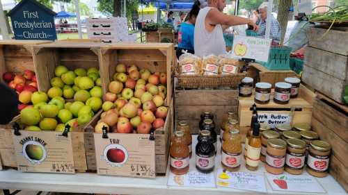 A market stall displays crates of apples and jars of apple butter, with a sign for the First Presbyterian Church.