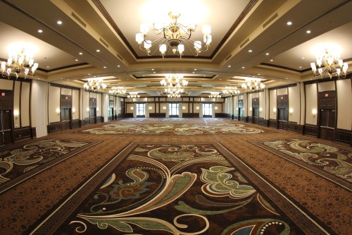 A spacious, elegantly designed banquet hall with chandeliers and ornate carpet patterns.