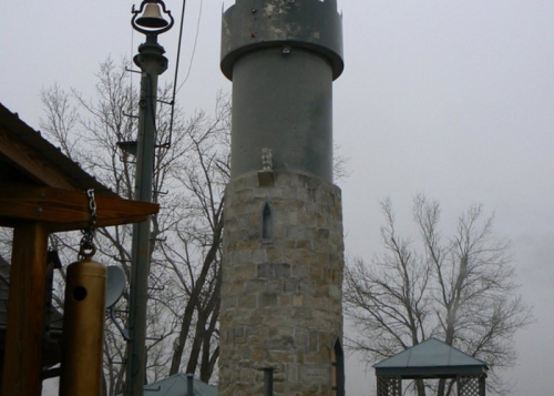 A tall stone tower with a gray metal top, surrounded by bare trees and a foggy atmosphere.