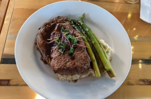A plate featuring a slice of beef steak, asparagus, and creamy mashed potatoes, garnished with microgreens.