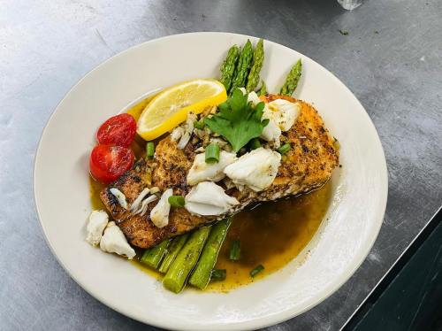 Grilled salmon topped with crab, served with asparagus, cherry tomatoes, and a lemon wedge on a white plate.