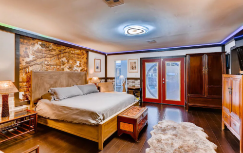 A spacious bedroom featuring a large bed, wooden furniture, decorative lamps, and a round door.