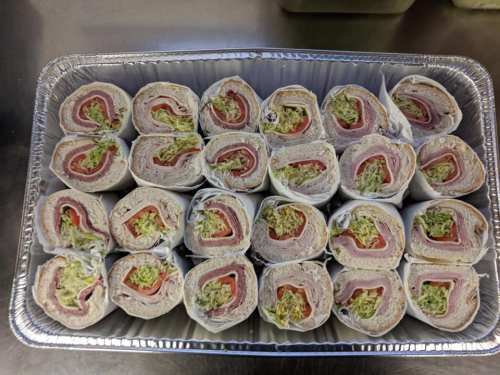 A tray of neatly arranged rolled sandwiches with layers of meat and lettuce, ready to serve.