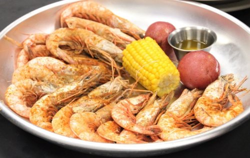 A metal platter filled with seasoned shrimp, corn on the cob, and red potatoes, accompanied by a small bowl of sauce.