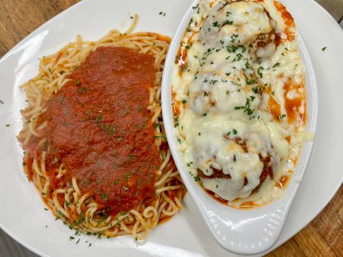 A plate of spaghetti with marinara sauce and a dish of cheesy meatballs, garnished with parsley.