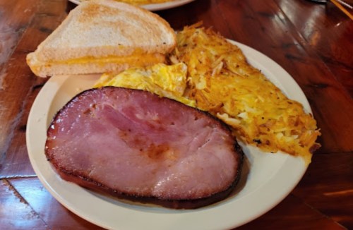 A plate with ham, a cheese sandwich, and crispy hash browns, served on a wooden table.