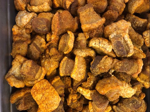 A close-up of a pile of crispy, golden-brown pork cracklings, seasoned and ready to eat.