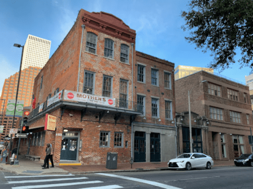 Historic brick building with a sign for "Mother's" restaurant, located at a city intersection with modern buildings in the background.