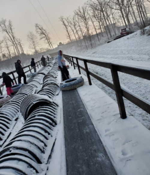 People walking on a snowy path beside a line of inflatable tubes, with trees in the background.