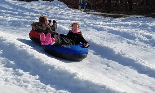 Two children slide down a snowy hill on colorful inner tubes, enjoying a winter day.