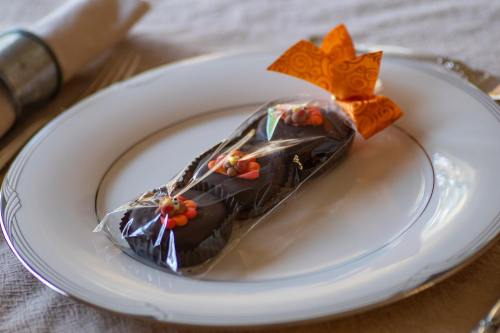A decorative chocolate treat wrapped in clear plastic, placed on a white plate with an orange bow.
