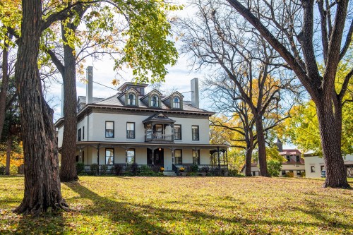 A large, historic house surrounded by trees and autumn foliage on a sunny day.