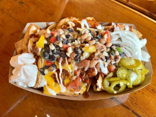A tray of nachos topped with cheese, beans, salsa, onions, jalapeños, and sour cream on a wooden table.
