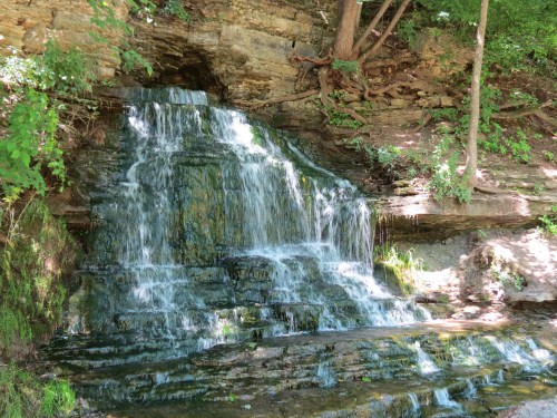 A serene waterfall cascading over rocky terrain, surrounded by lush greenery and trees.