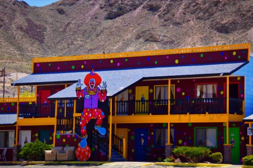 Colorful motel with a large clown mural on the exterior, set against a mountainous backdrop.