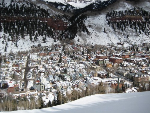 A snowy mountain town nestled in a valley, surrounded by trees and mountains, with colorful buildings and rooftops.