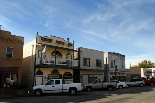 Historic buildings line a street under a blue sky, featuring a balcony and an American flag.