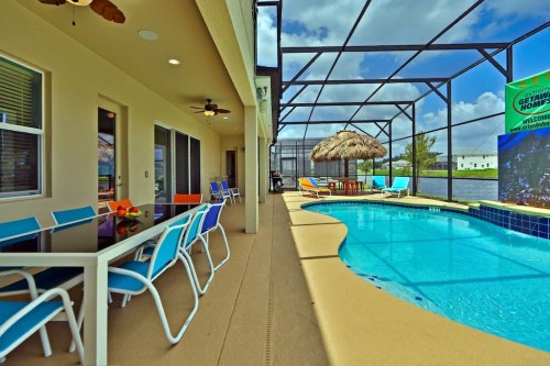 A sunny patio with colorful chairs, a pool, and a thatched umbrella, surrounded by a screened enclosure.