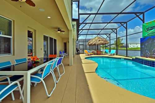 A sunny patio with colorful chairs, a pool, and a thatched umbrella, surrounded by a screened enclosure.