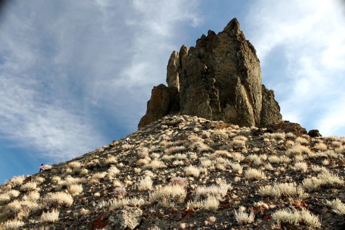 A rocky outcrop rises from a dry, grassy landscape under a blue sky with scattered clouds.