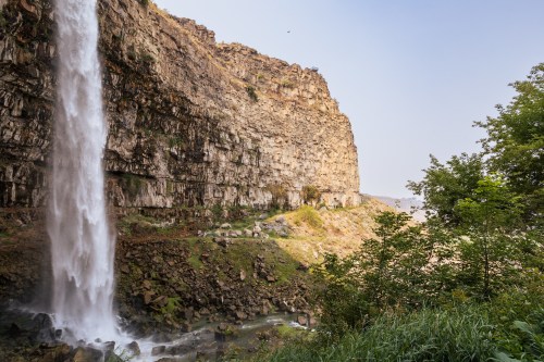 A majestic waterfall cascading down a rocky cliff, surrounded by lush greenery and a serene landscape.