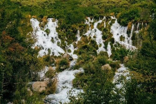 A cascading waterfall surrounded by lush greenery and rocky terrain, creating a serene natural landscape.