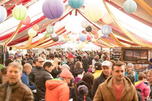 A bustling indoor market filled with people, colorful lanterns hanging from the ceiling, and vibrant decorations.