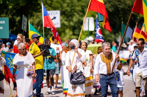A diverse group of people in colorful attire march in a parade, holding flags and celebrating cultural heritage.