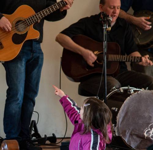 A child points excitedly at musicians playing guitar and drums during a live performance.