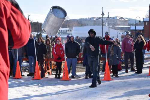 A crowd watches as a person throws a barrel in a snowy outdoor event, with orange cones marking the area.