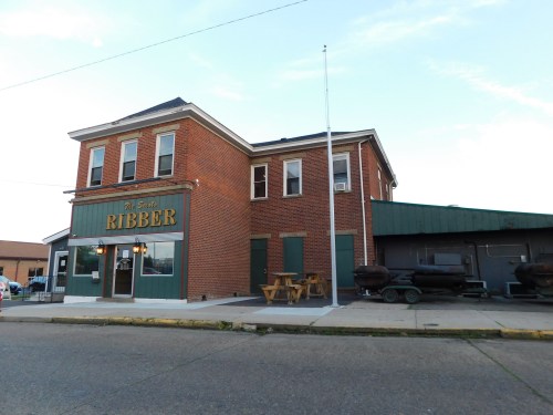 A brick building with "Ribber" signage, featuring outdoor seating and a green awning, set on a quiet street.