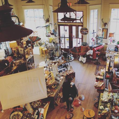 A cozy shop filled with various antiques, decor items, and unique artifacts, featuring warm lighting and wooden floors.