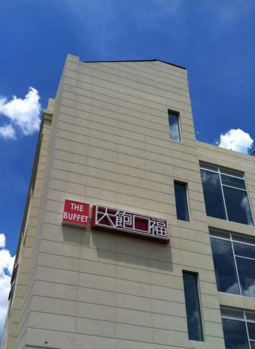 A modern building with a sign reading "The Buffet" in English and Chinese against a blue sky with clouds.