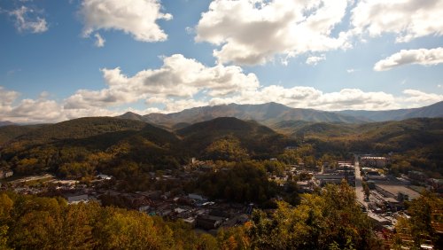 A panoramic view of a mountainous landscape with a town nestled in the valley, under a partly cloudy sky.