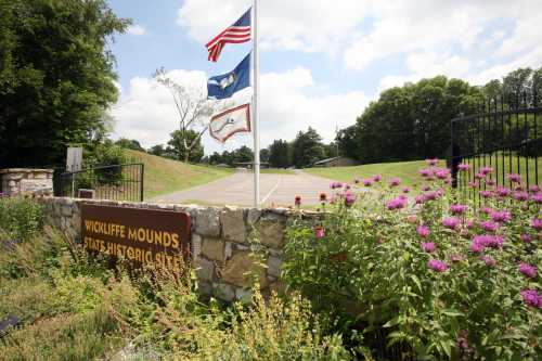 Entrance to Wickliffe Mounds State Historic Site, featuring flags and colorful flowers in a scenic landscape.