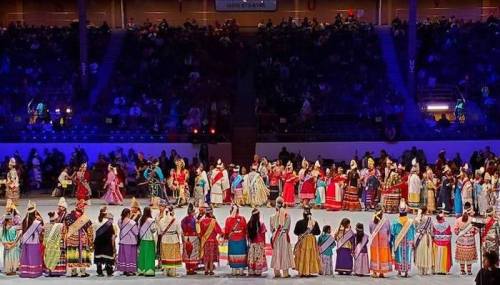 A vibrant cultural performance featuring a large group of dancers in traditional attire on a stage with an audience.
