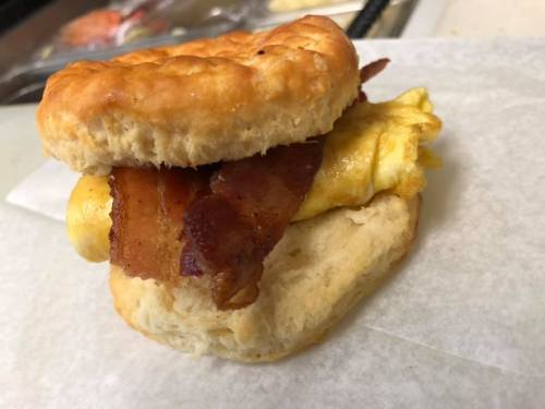 A biscuit sandwich filled with crispy bacon and a fluffy omelet, resting on a piece of parchment paper.