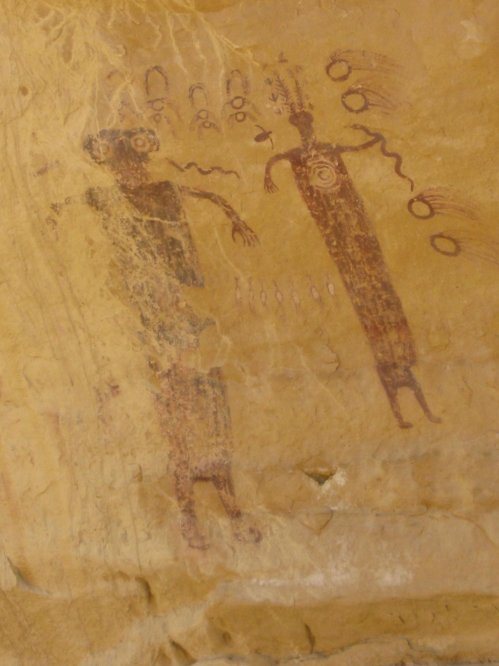 Ancient rock art depicting two figures with circular patterns and wavy lines on a textured stone surface.
