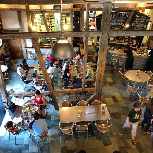 A bustling café with wooden beams, tables filled with people, and a counter serving food and drinks.
