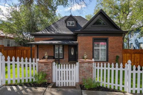 A charming brick house with a black roof, surrounded by a white picket fence and lush green grass.