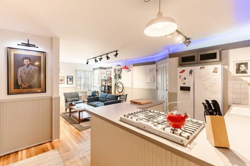 A modern kitchen opens to a cozy living area, featuring artwork, a bicycle, and stylish furniture.