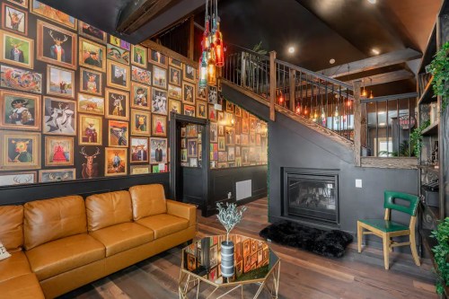 Cozy living space with a brown leather sofa, colorful gallery wall, and modern decor, featuring a fireplace and staircase.